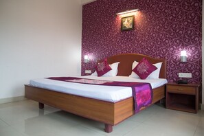 A bedroom with a wooden bed, two bedside tables, and patterned wallpaper. - Hotel New Rockbay (Puri)