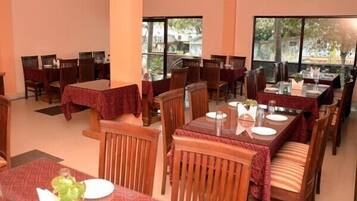 A restaurant with multiple tables and chairs, large windows, and a view of greenery outside.