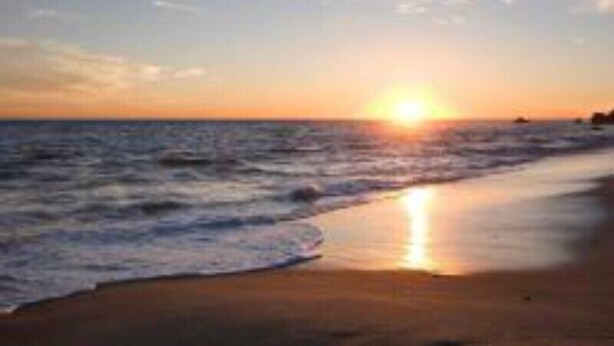 Una playa al atardecer con el sol cerca del horizonte, mar tranquilo y cielo despejado.