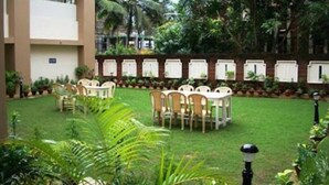 Un patio con zona de comedor, rodeado de plantas en macetas y un edificio con fachada de ladrillo.