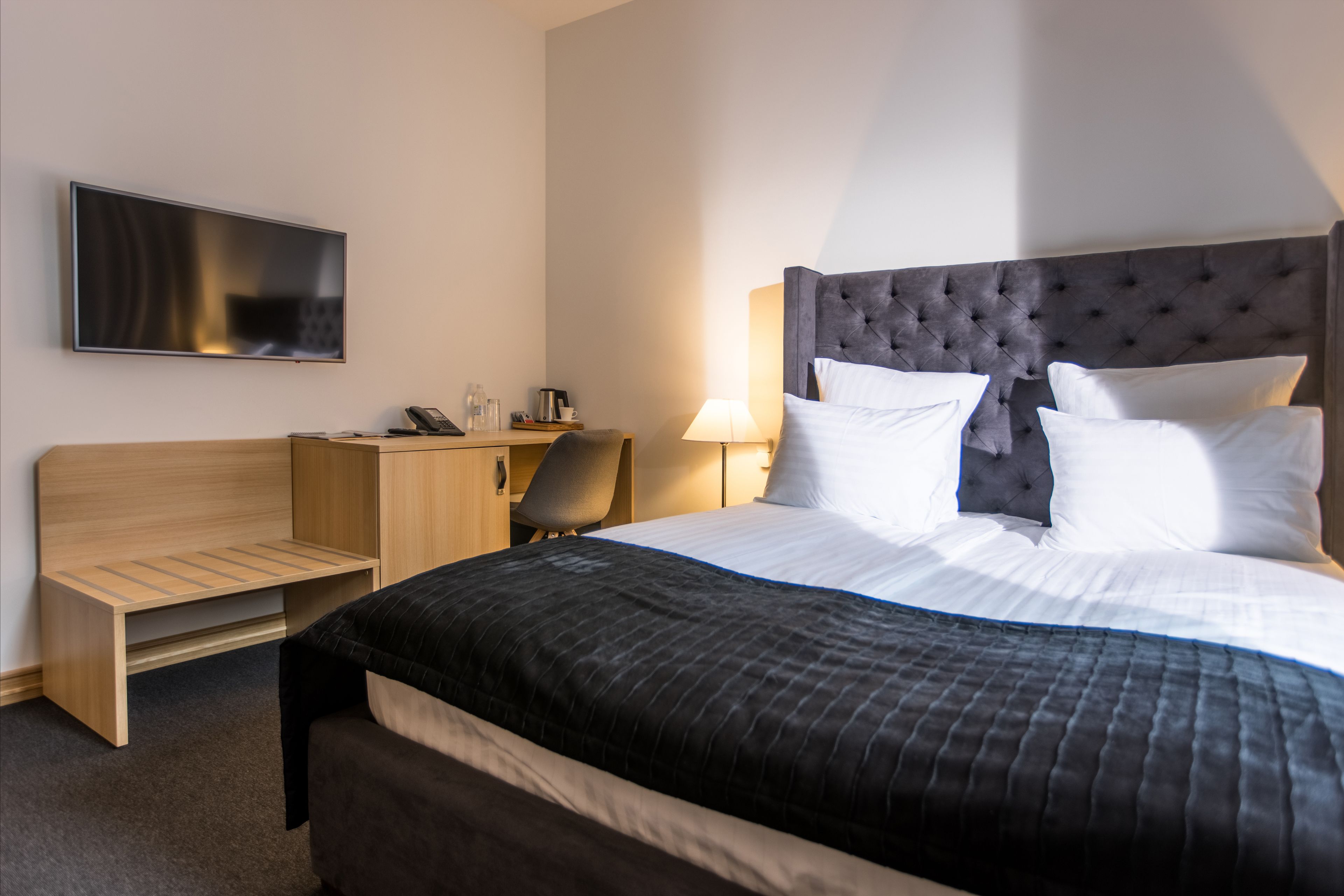 A hotel room with a bed, a desk, a chair, a TV, and a lamp.