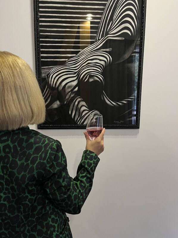A person holding a glass of wine in front of a framed artwork.
