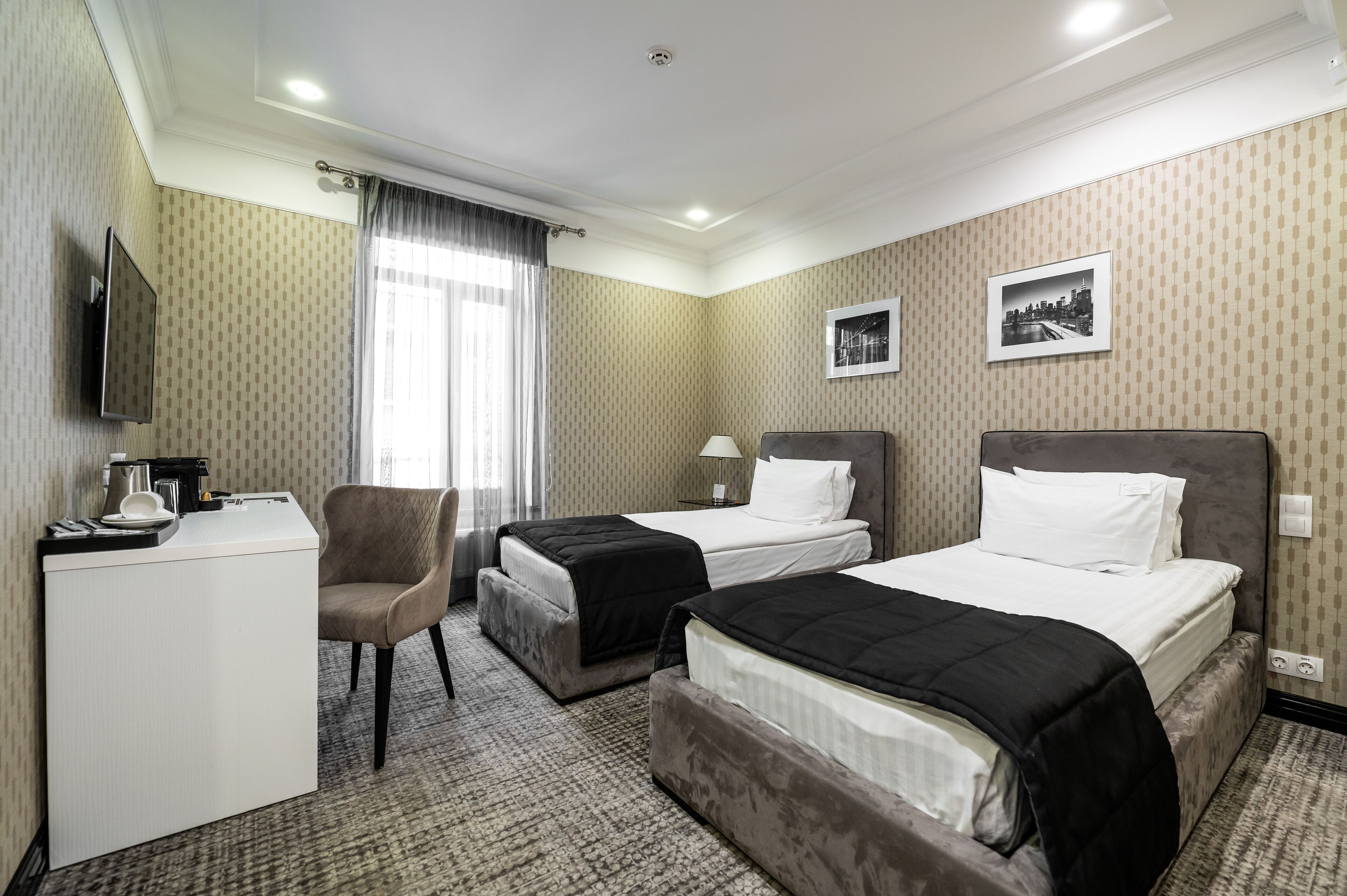 Une chambre d’hôtel avec deux lits, un bureau, une chaise, une télévision et une fenêtre avec des rideaux.