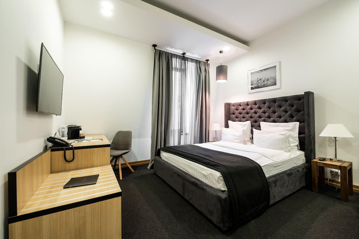 Habitación de hotel con cama, escritorio, silla, televisor y ventana con cortinas.