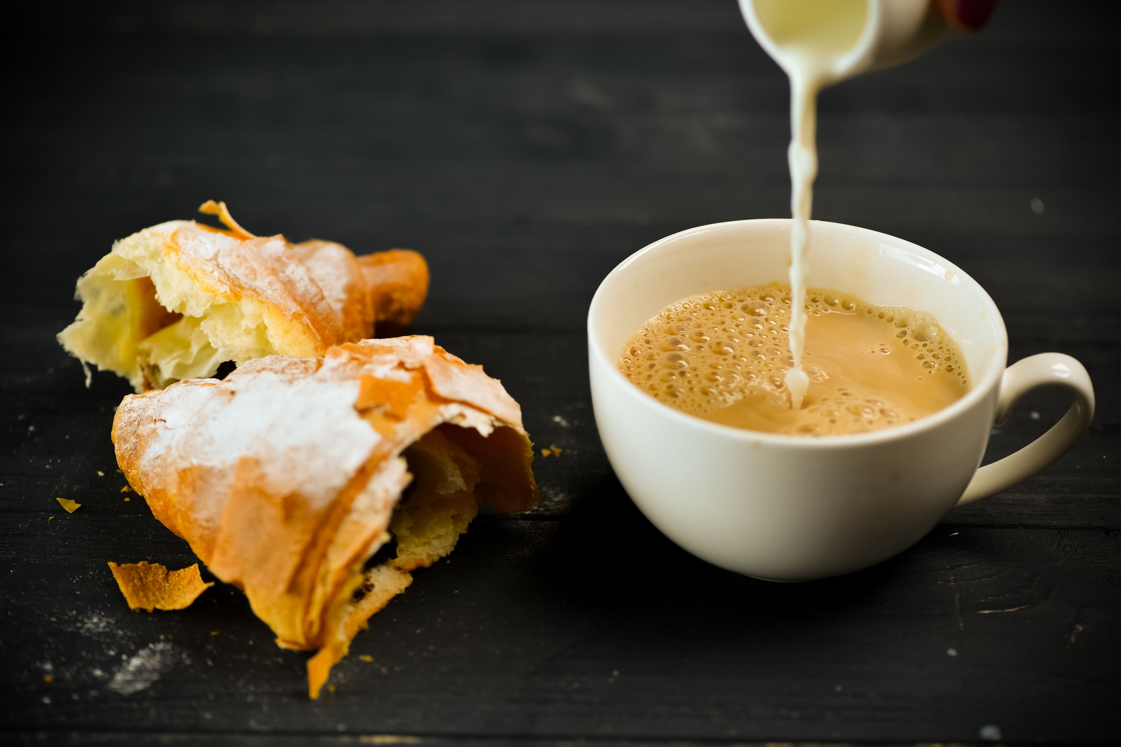 A cup of coffee with a pastry on a dark surface.