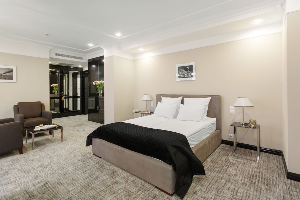 Habitación de hotel con una cama grande, un sofá, una mesita y una mesita de noche con lámparas.
