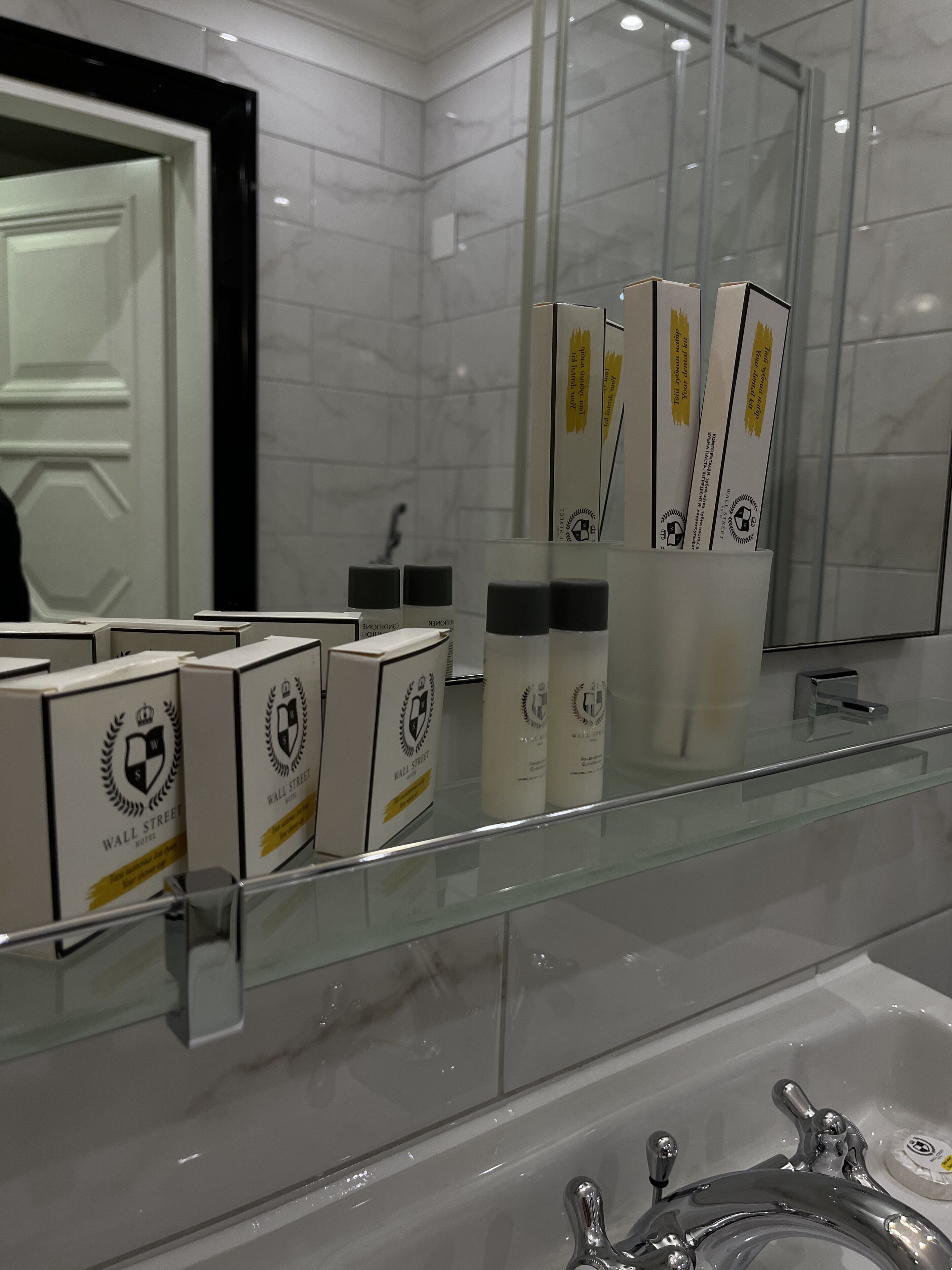 Un baño con repisa de vidrio que muestra artículos de aseo, un espejo y una bañera.