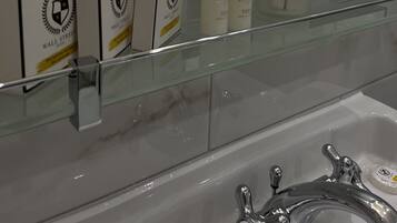 Un baño con repisa de vidrio que muestra artículos de aseo, un espejo y una bañera.