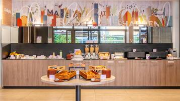 Um buffet de café da manhã moderno com diversos alimentos e um mural com vista para a cidade.