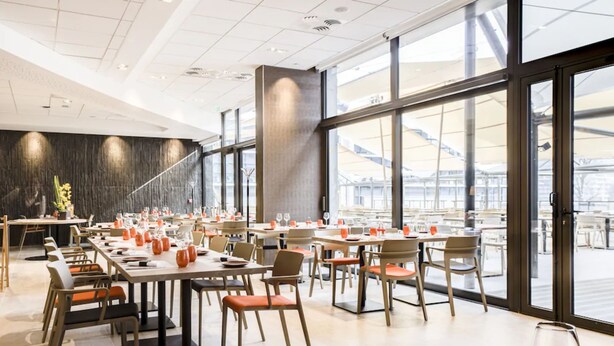 Un comedor moderno con varias mesas y sillas, ventanas amplias y vistas a la ciudad.