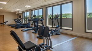 Un gimnasio con equipo de ejercicio, ventanas amplias y vistas a zonas verdes.