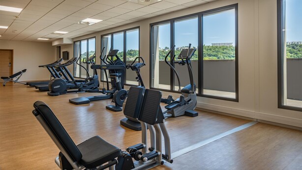 Et fitnesscenter med træningsudstyr, store vinduer og udsigt til grønne områder.