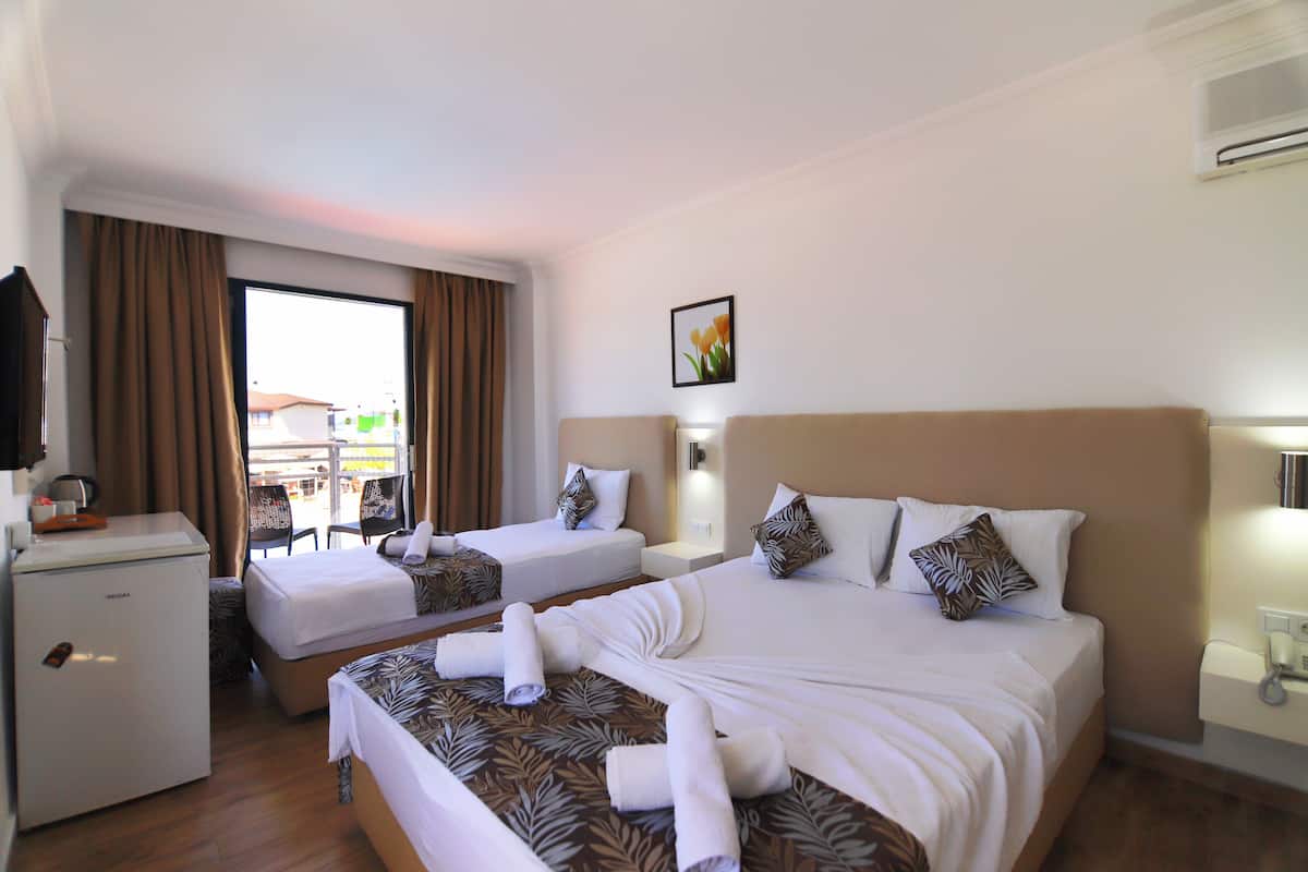 Habitación de hotel con dos camas, un escritorio, un refrigerador y una ventana con cortinas.