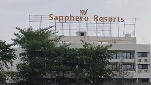 Een bord voor Sapphero Resorts met een modern gebouw op de achtergrond.