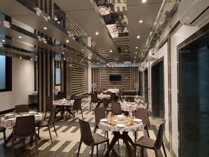 Een moderne eetruimte met meerdere tafels en stoelen, een flatscreen televisie aan de muur en airconditioningsystemen.