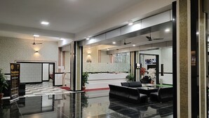 Een moderne hotellobby met een zwart-wit schachbordvloer, een receptiebalie, een zithoek en een grote spiegel die het interieur weerkaatst.