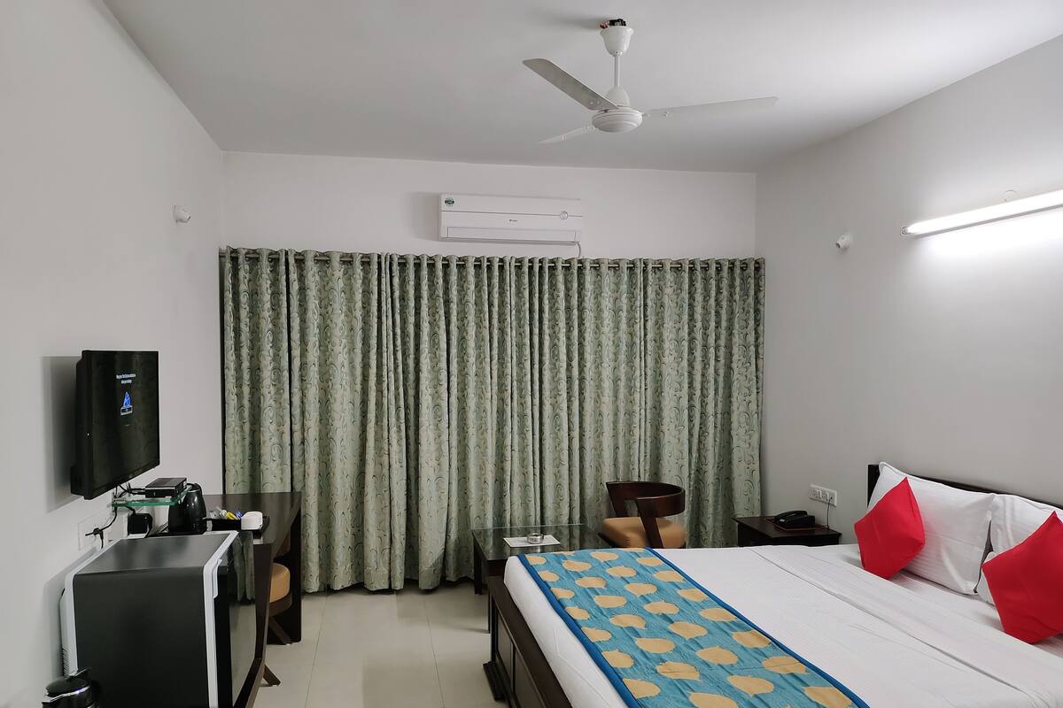 Een hotelkamer met een bed, een bureau, een stoel, een televisie en een airconditioner.