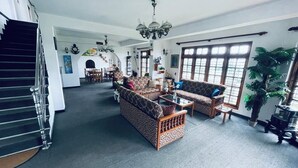 A spacious living room with a staircase, two patterned sofas, a coffee table, and a large window with a view. - Royal Mount Hotel (Nuwara Eliya)