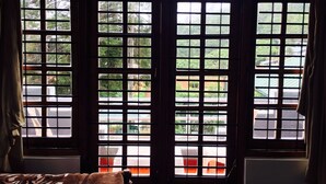 A room with large windows featuring a grid pattern, curtains, and a view of greenery outside. - Royal Mount Hotel (Nuwara Eliya)