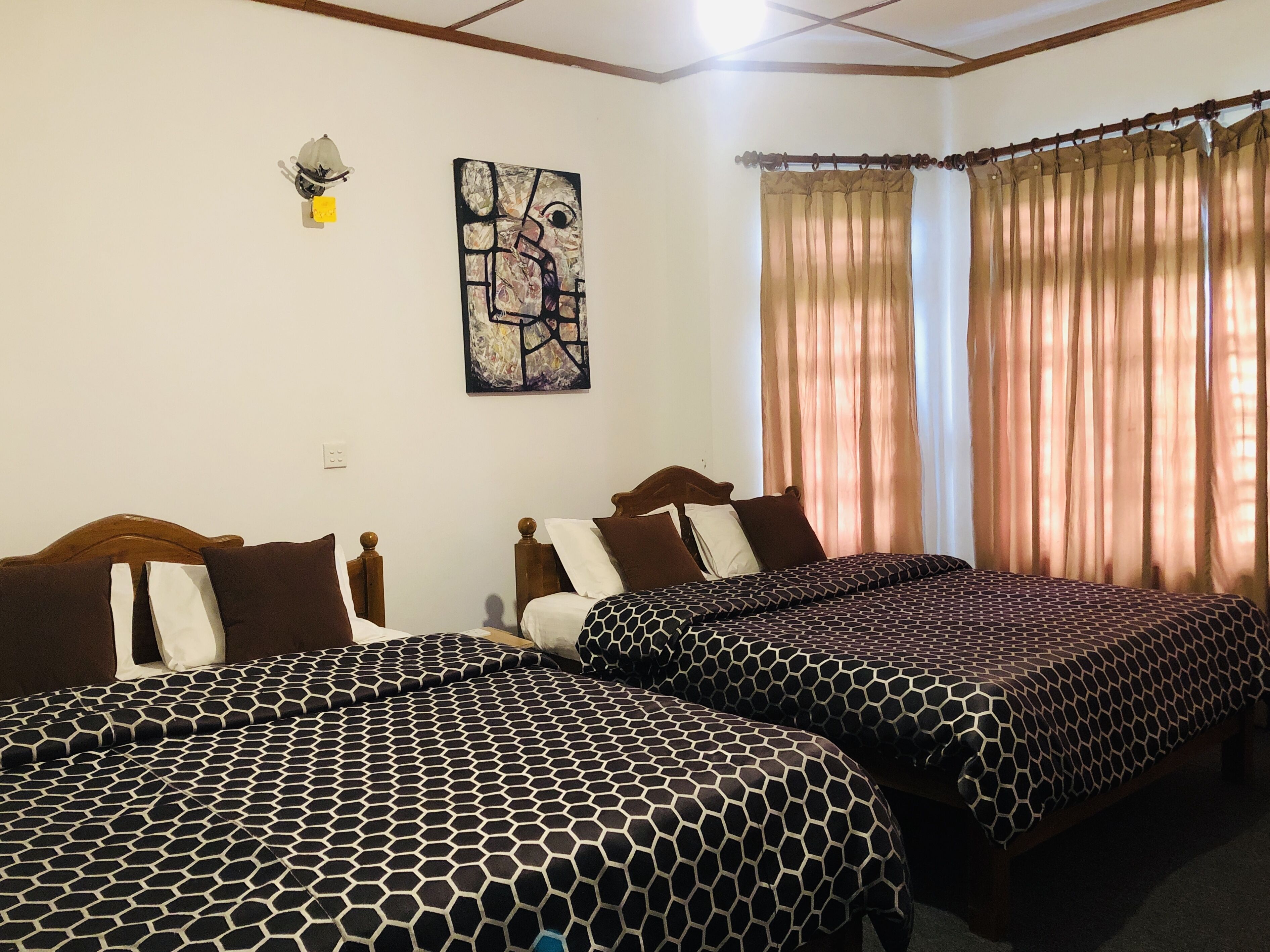 A hotel room with two beds, a painting on the wall, and curtains on the windows.