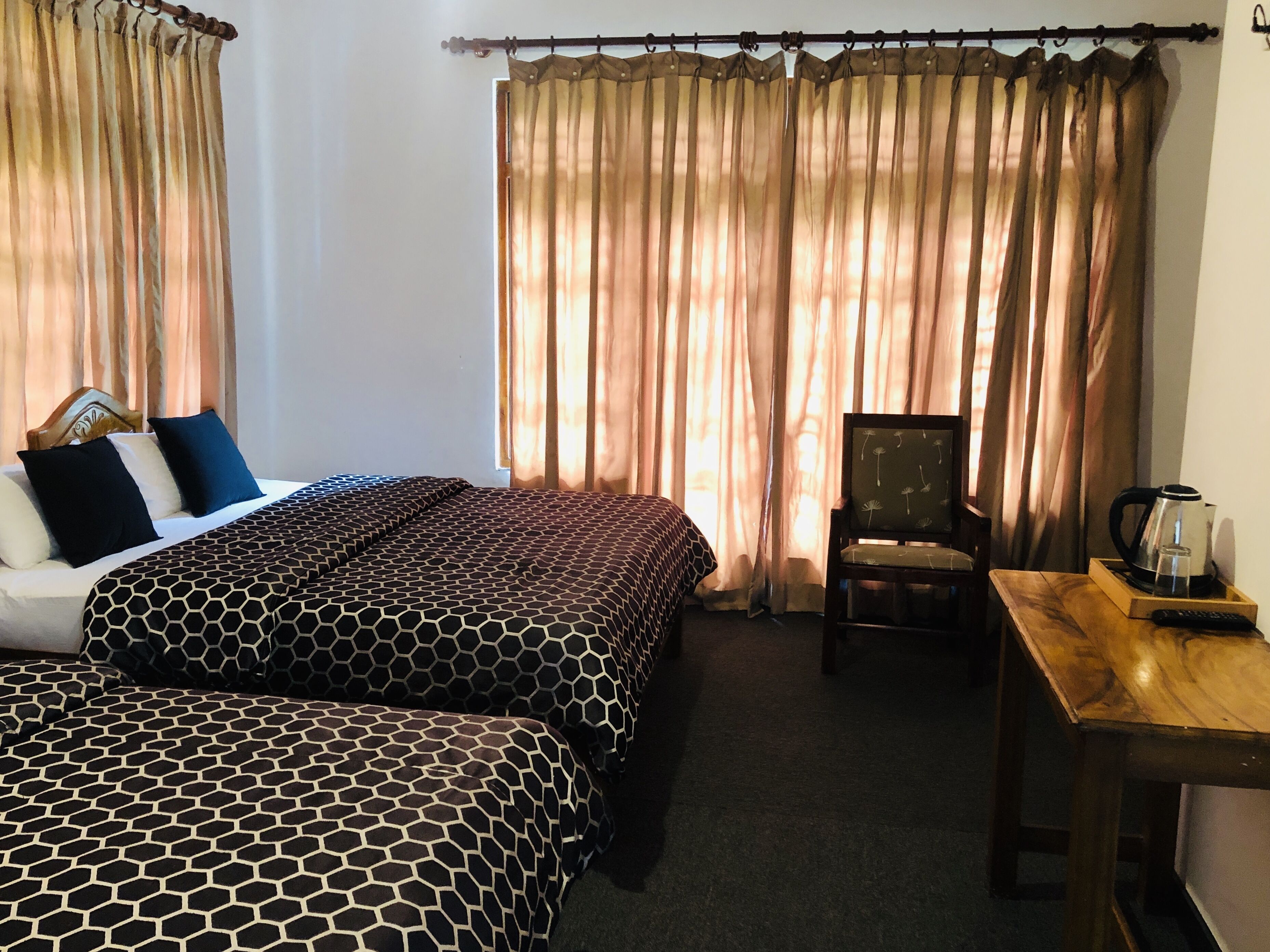 A hotel room with two beds, a wooden table with a kettle, and a chair.