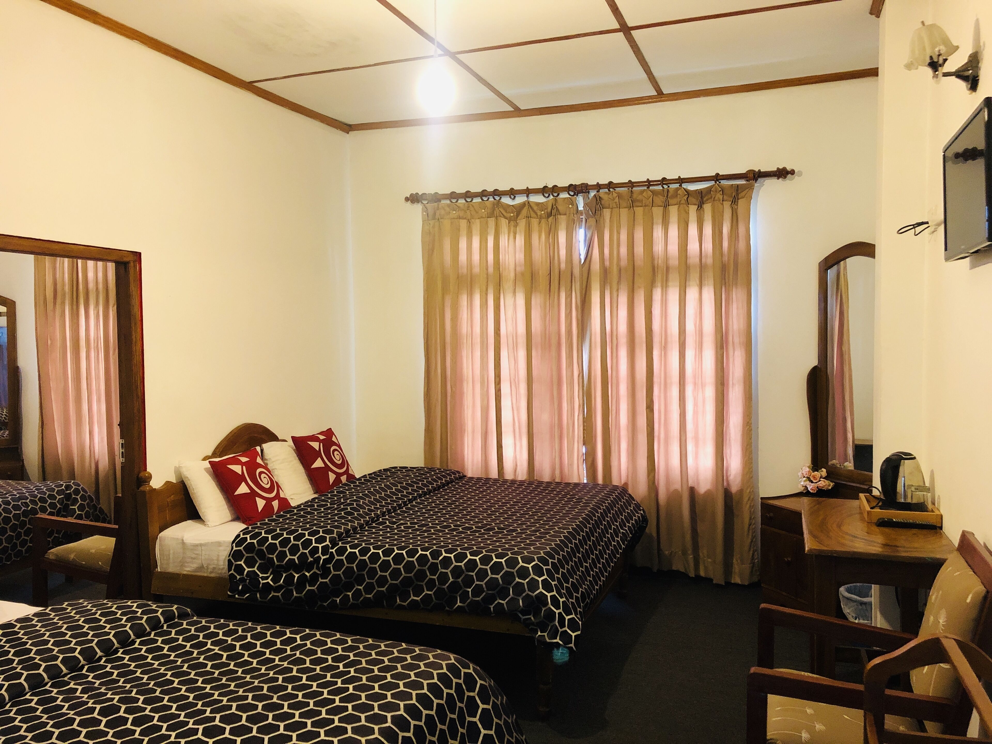 A hotel room with two beds, a wooden desk, a chair, a mirror, and a window with curtains.