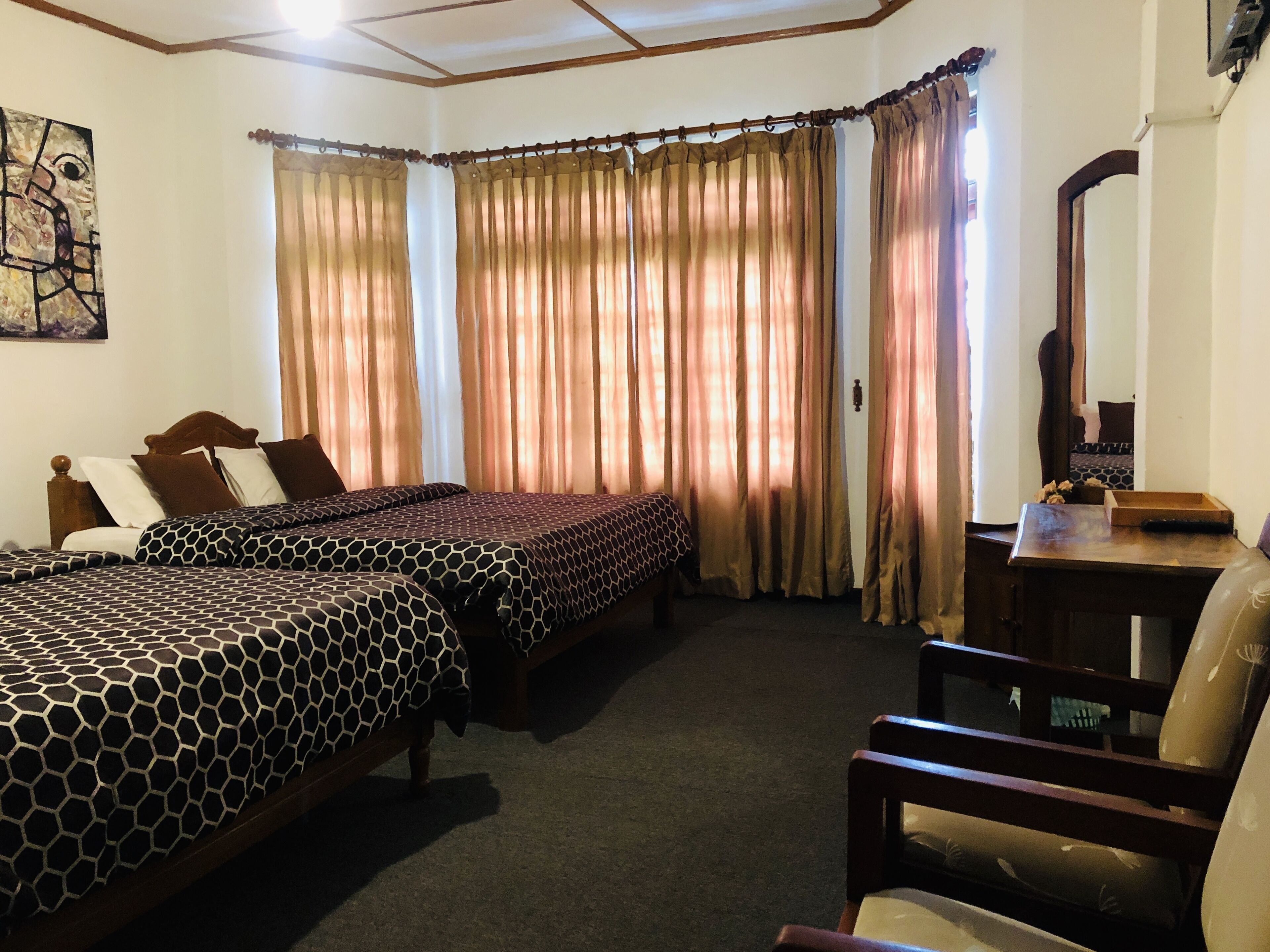 A hotel room with two beds, a desk, a chair, and a large window with curtains.