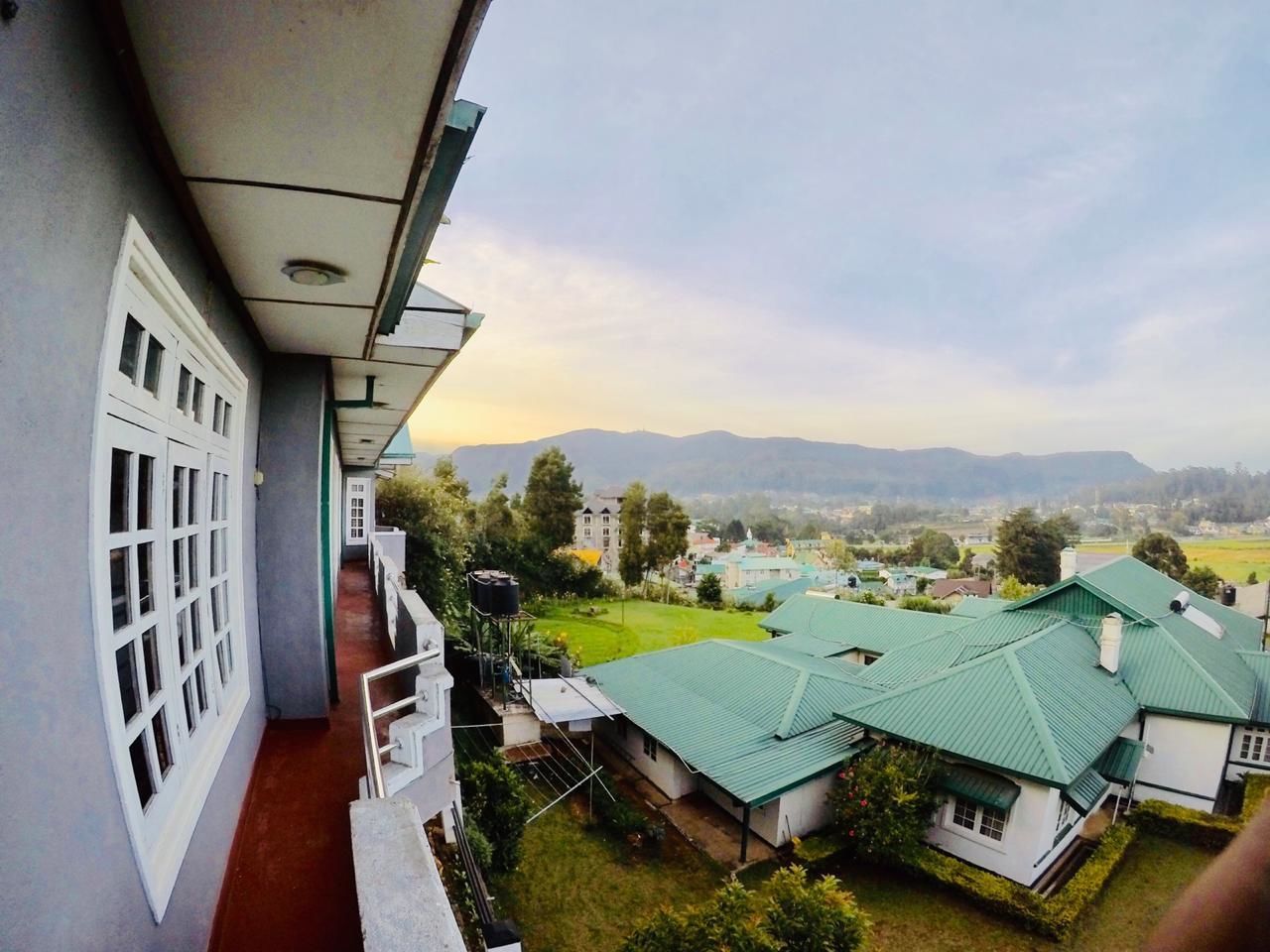 A view from a balcony overlooking a residential area with green-roofed houses and a distant mountain range.