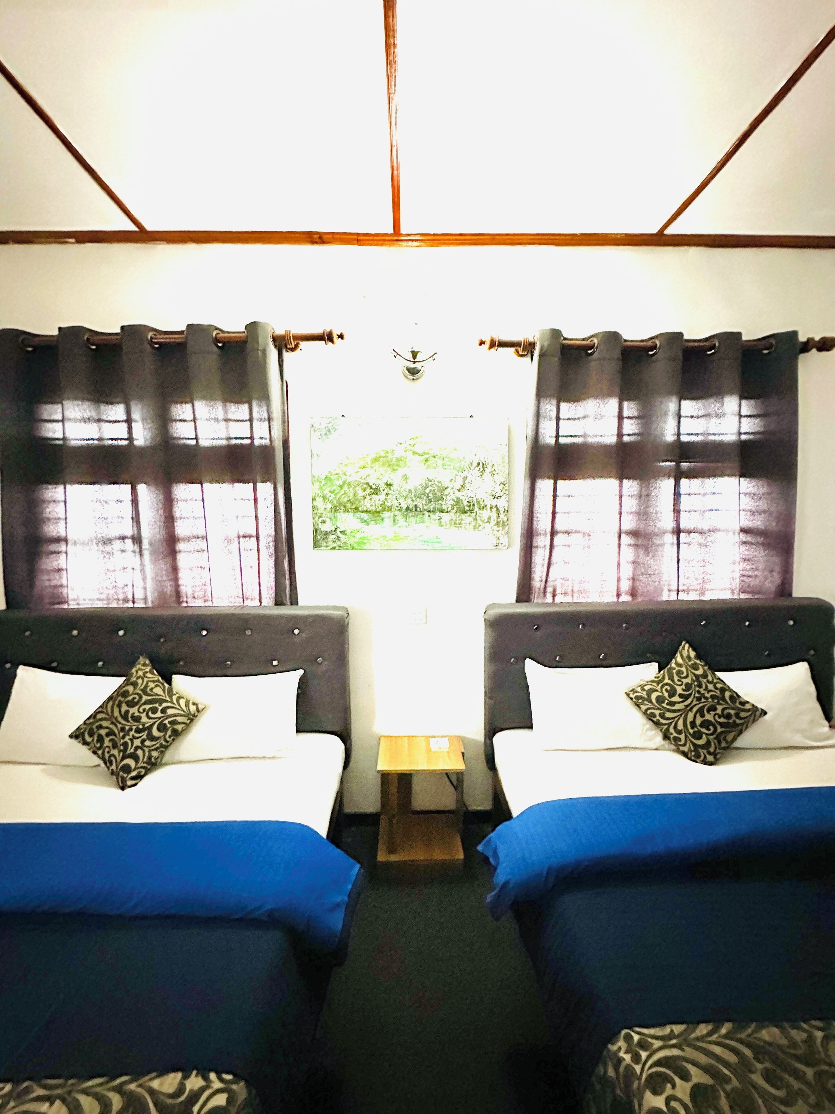 Ein Zimmer mit zwei Betten, jeweils mit Kissen und Kopfteil. Dazwischen steht ein kleiner Tisch.