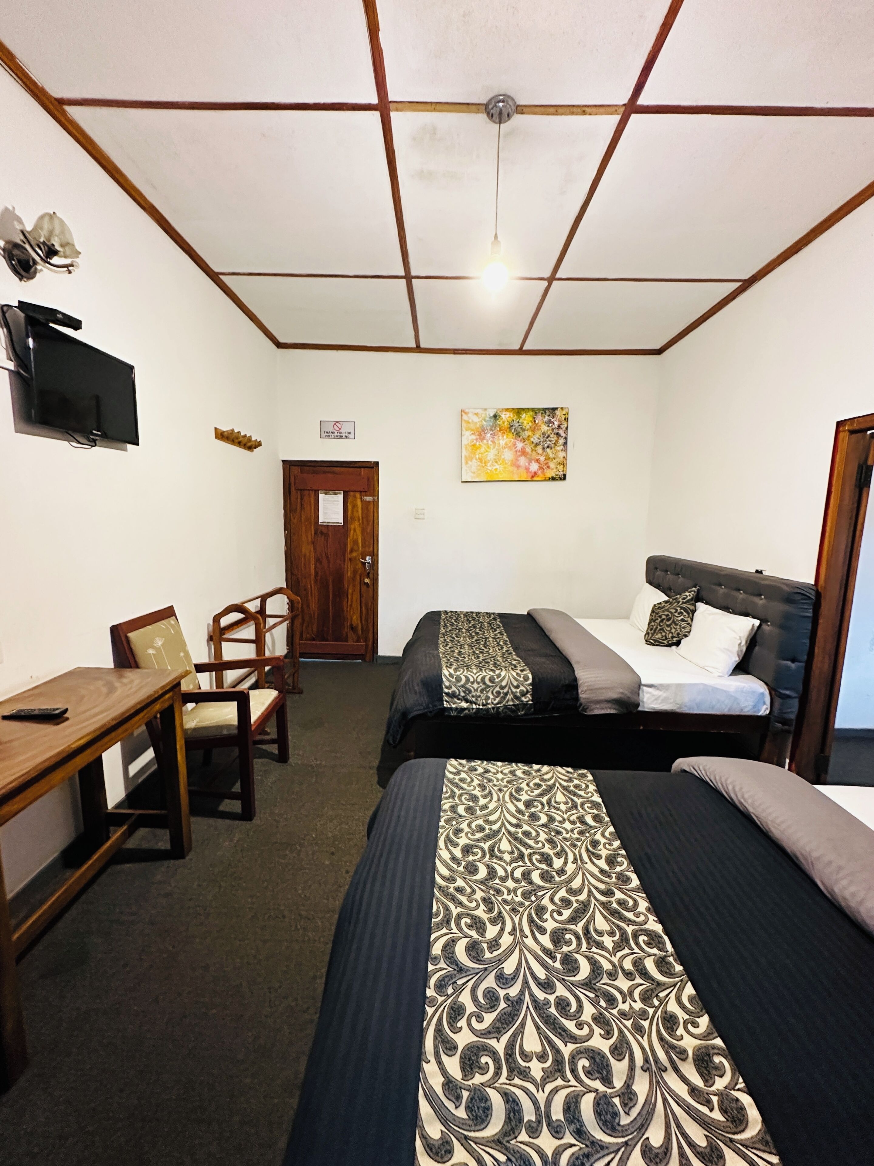 A room with two beds, a desk, a chair, a television, and a painting on the wall.