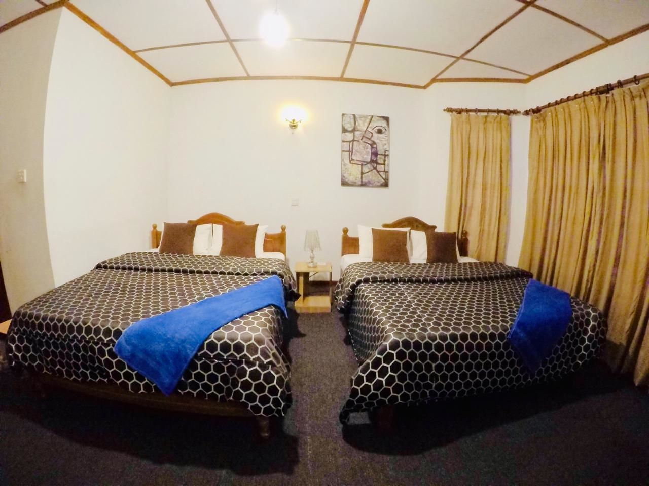 A hotel room with two beds, a nightstand, a lamp, and a painting on the wall.