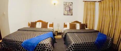 A hotel room with two beds, a nightstand, a lamp, and a painting on the wall.