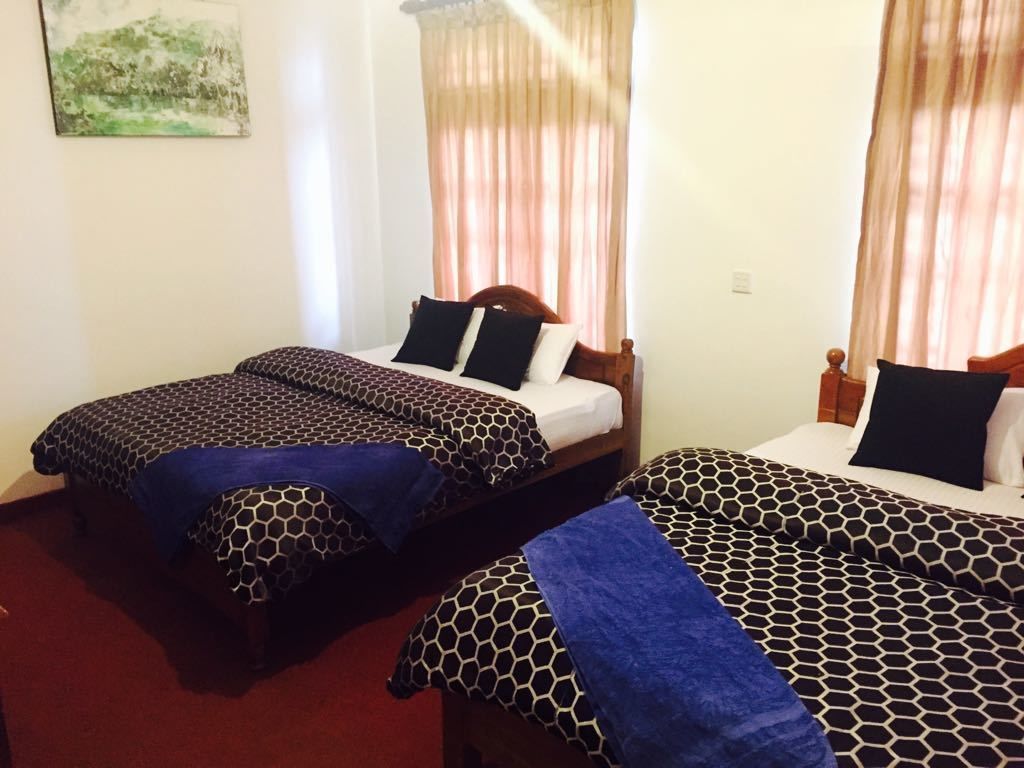 A hotel room with two single beds, each with a patterned bedspread and pillows, a wooden headboard, and a window with sheer curtains.