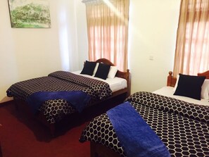 A hotel room with two single beds, each with a patterned bedspread and pillows, a wooden headboard, and a window with sheer curtains.