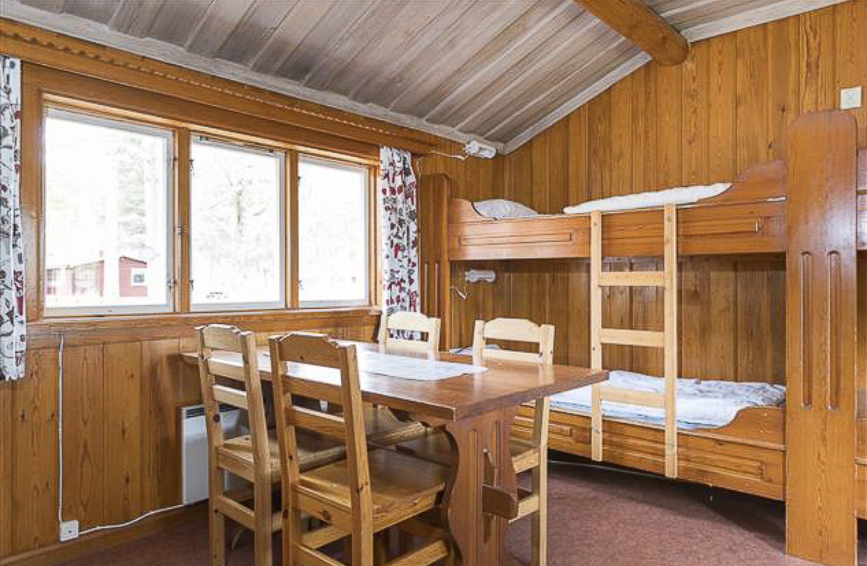 Una cabaña de madera con literas, una mesa de comedor y sillas.