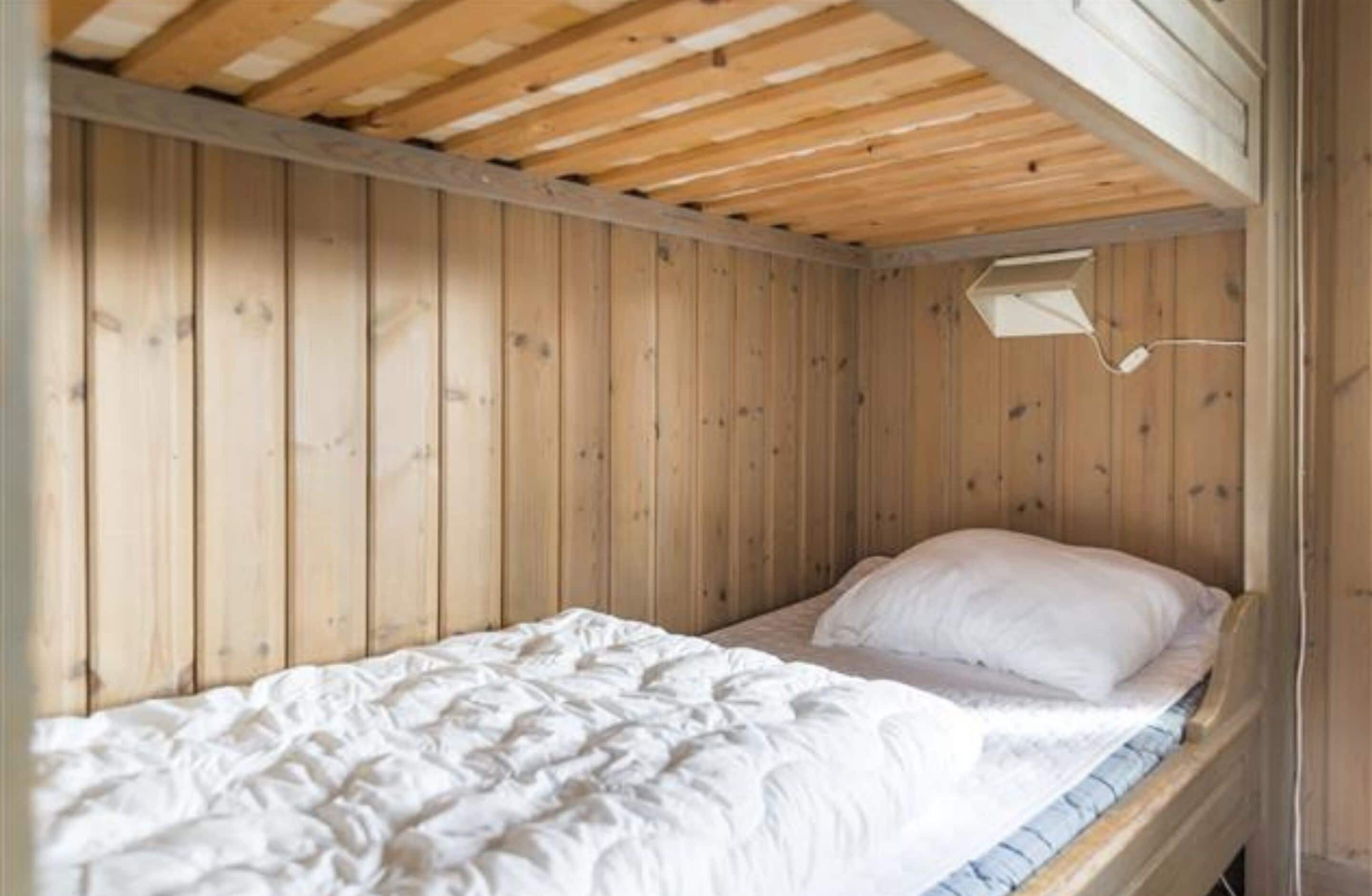 A single bed with a white mattress and pillows in a room with wooden walls and a sloped ceiling.