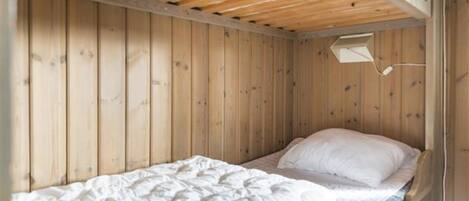 A single bed with a white mattress and pillows in a room with wooden walls and a sloped ceiling.