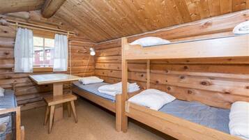 A wooden cabin room with bunk beds, a small table, and a window with curtains.