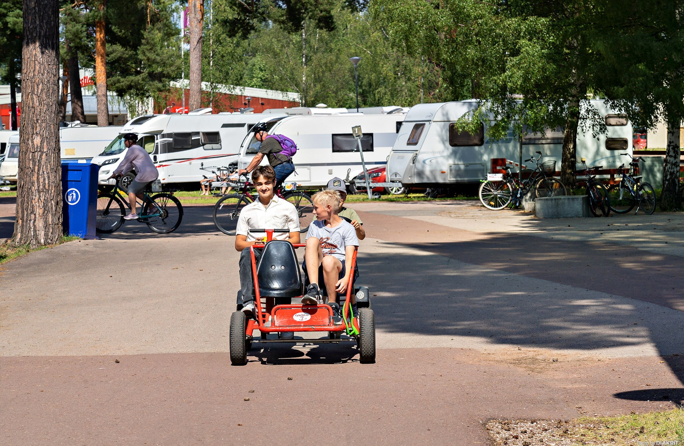 Un chemin pavé, avec en arrière-plan un kart rouge, des vélos et des camping-cars.