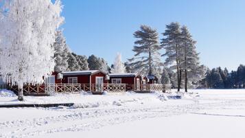 A snow-covered landscape with a red cabin and tall trees.