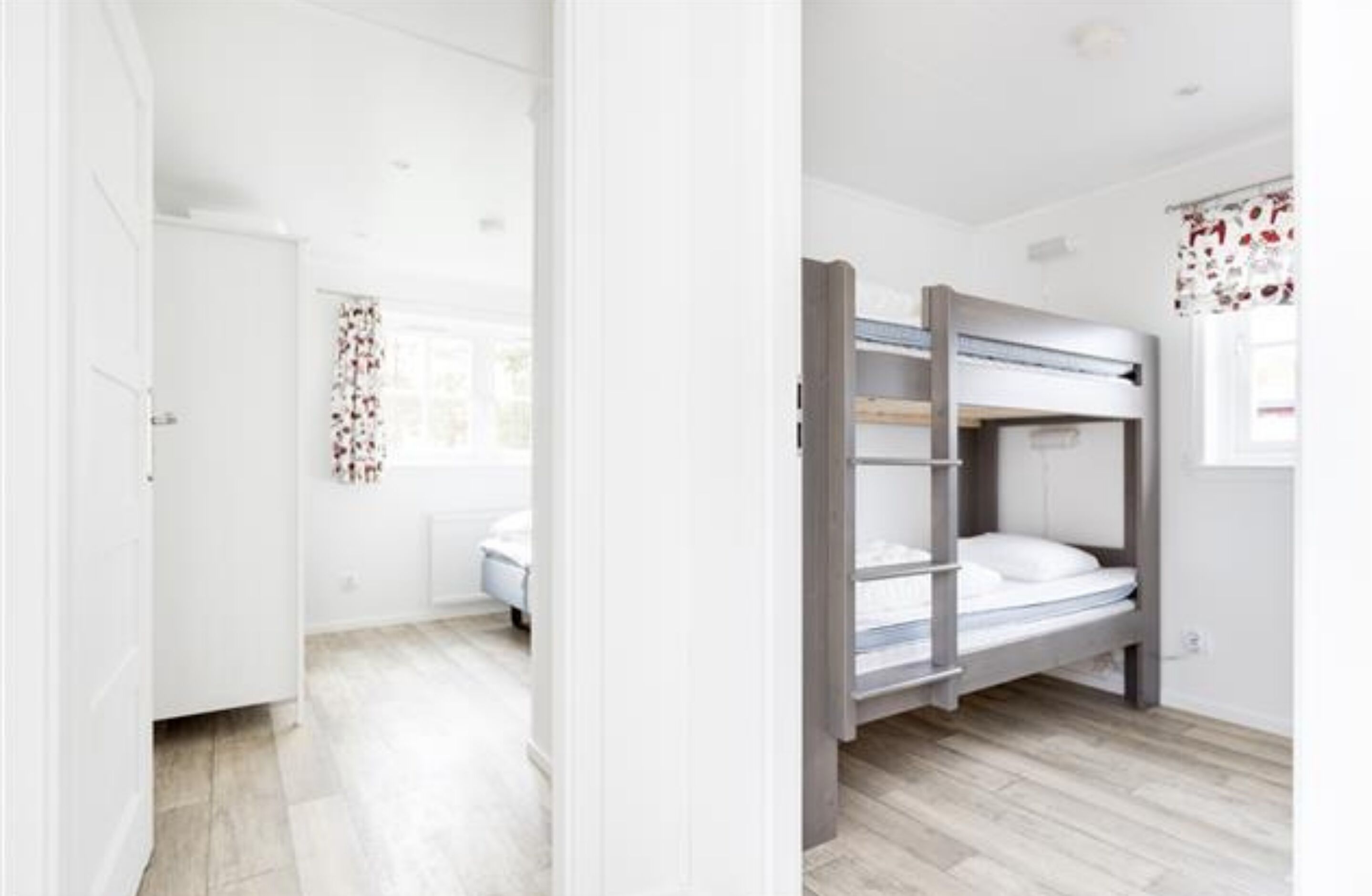 A room with a bunk bed, a small desk, and a window with floral curtains.