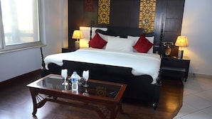 A hotel room with a large bed, two bedside tables with lamps, a glass coffee table, and a view of the outside through a window. - Gofas Lodge (Islamabad)