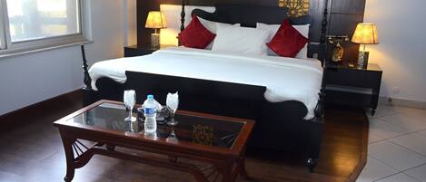 Habitación de hotel con una cama grande, dos mesitas de noche con lámparas, una mesa de centro de cristal y vistas al exterior por una ventana.