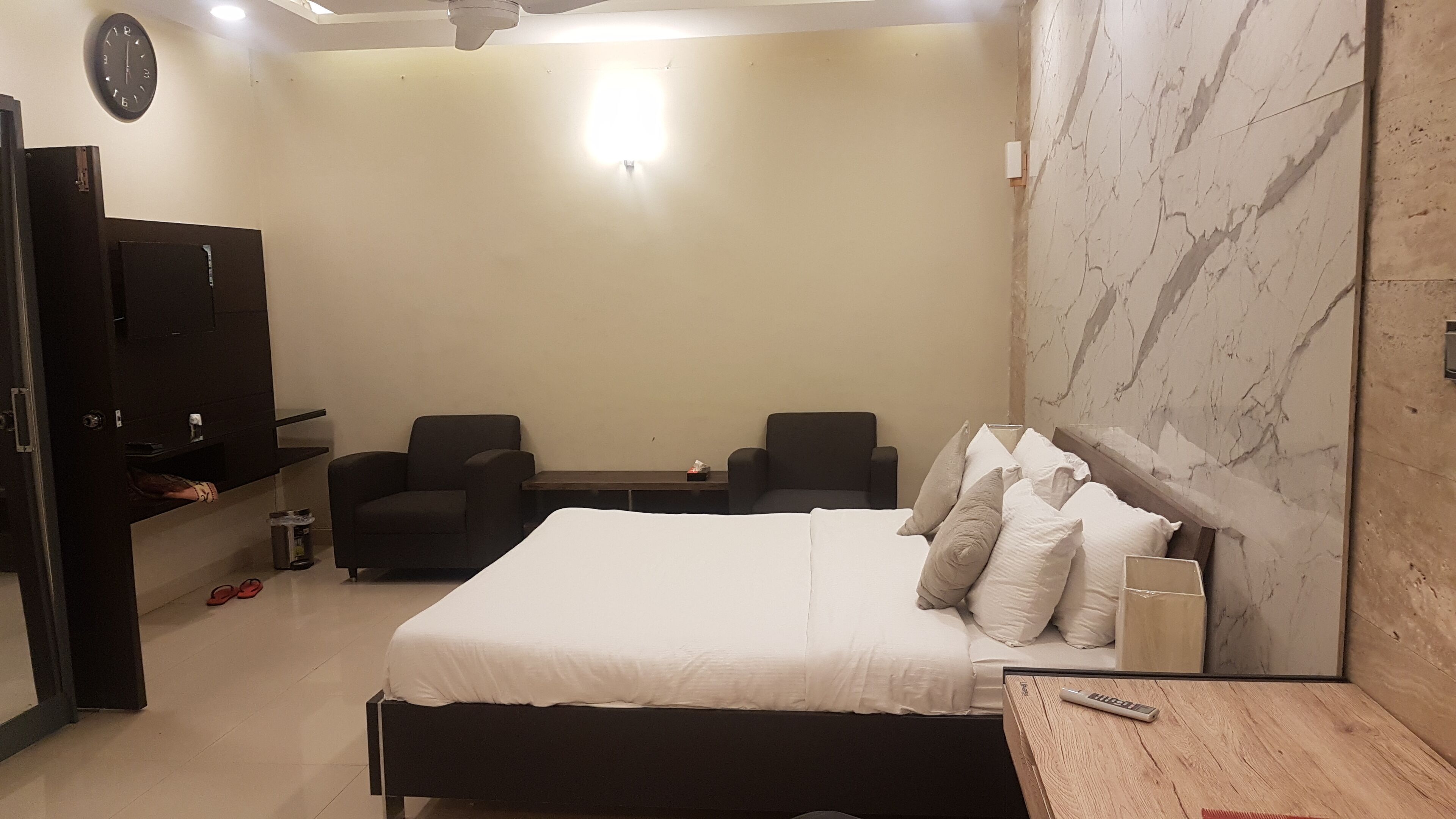 Une chambre moderne avec un grand lit, deux fauteuils, une télévision et un mur en marbre.
