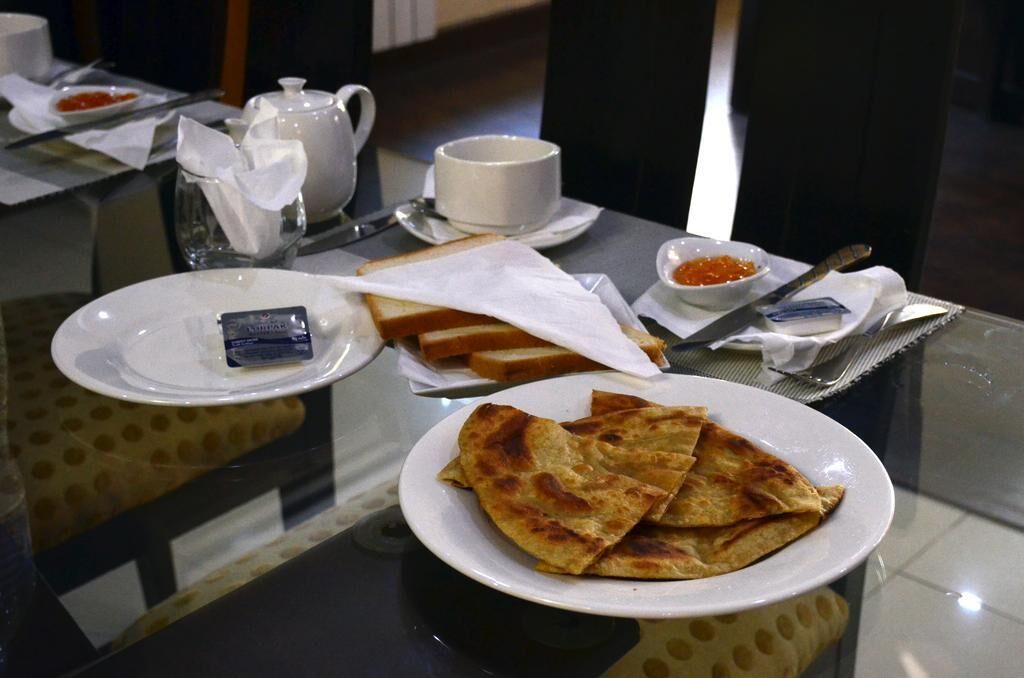 A dining table with a plate of flatbreads, a cup, a teapot, and a small bowl of red condiment.