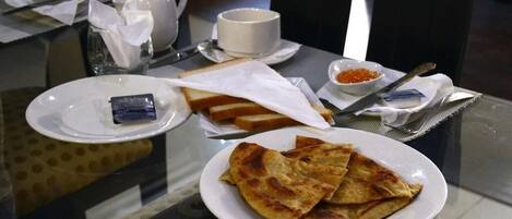 A dining table with a plate of flatbreads, a cup, a teapot, and a small bowl of red condiment.