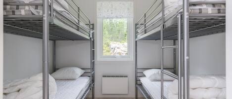 Een slaapzaal met stapelbedden, een raam met uitzicht op groen, en een radiator.
