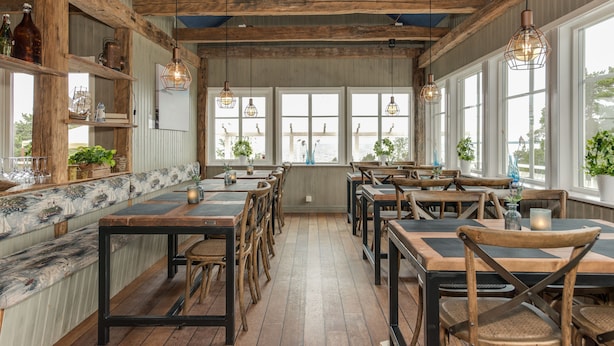 Un interior rústico con vigas de madera, ventanas amplias y una larga zona de asientos tipo banco.