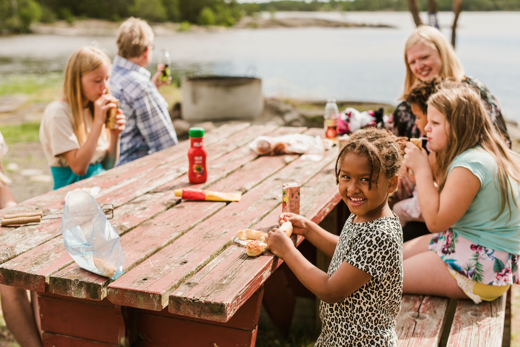 A group of people sitting at a wooden picnic table by a lake.