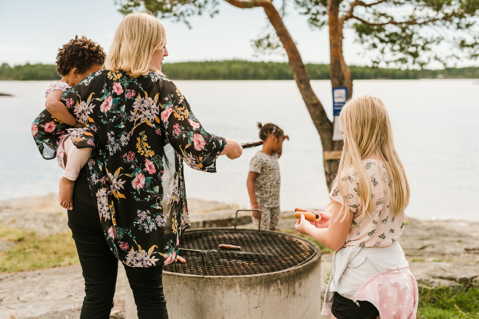A group of people gathered around a grill by a lake.